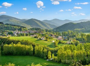 A rural landscape with a small village, green fields, and mountains in the background.