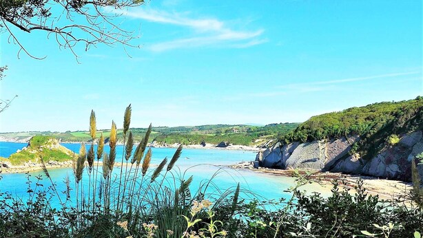 Paesaggio costiero con cielo azzurro intenso, scogliere rocciose e spiaggia sabbiosa.
