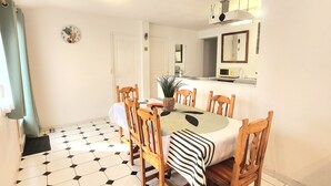 A dining area with a hexagonal tiled floor, a round table with chairs, a kitchen area with a stove and sink, and a clock on the wall. - Homerez - Villa in Meynes (Meynes)