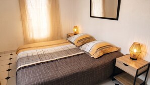 A bedroom with a bed, bedside table, lamp, mirror, and curtains. - Homerez - Villa in Meynes (Meynes)