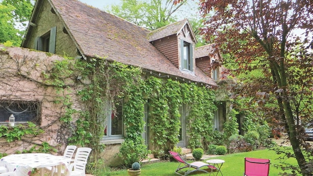 A stone house with a sloped roof, ivy-covered walls, and a small garden with a table, chairs, and a red chair. - Homerez - House in Saint Branchs (Saint Branchs)