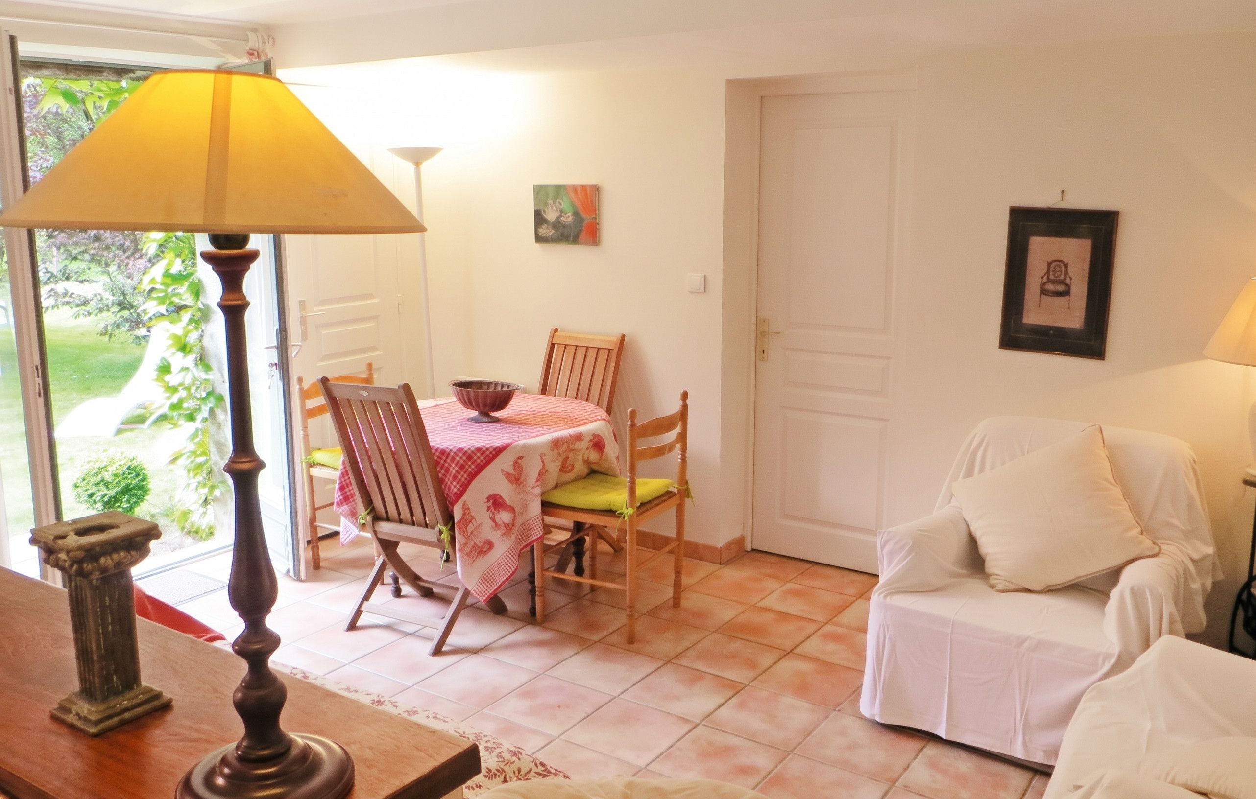 A dining area with a table set for two, a chair, a lamp, and a door leading outside.