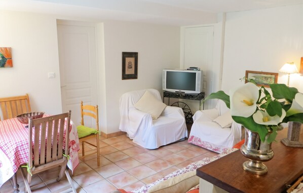 A room with two beds covered in white sheets, a television on a stand, a dining table with chairs, and a vase with flowers. - Homerez - House in Saint Branchs (Saint Branchs)