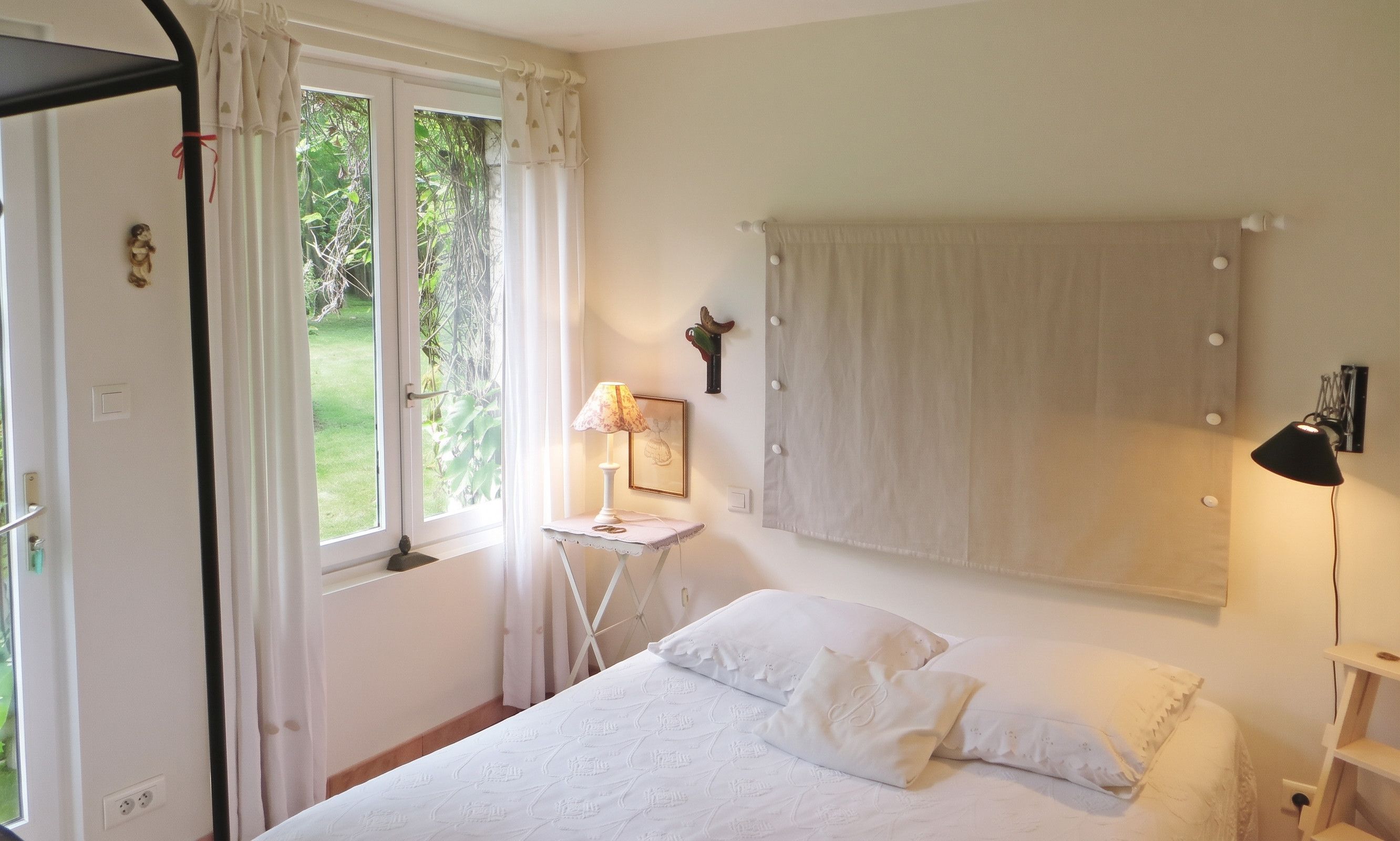 A bedroom with a bed, a bedside table with a lamp, a window with curtains, and a door.