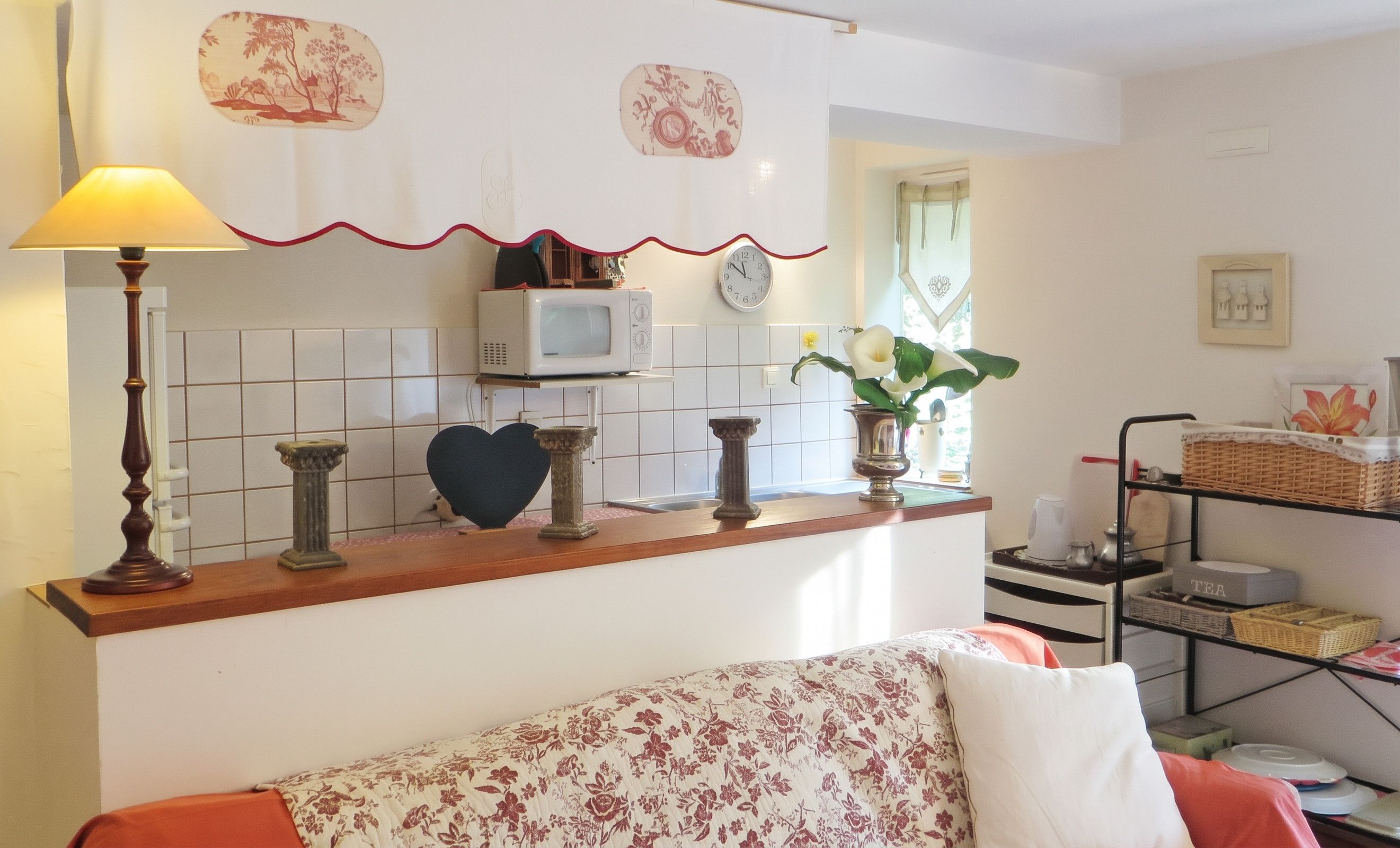 Una cocina con microondas, un reloj y una estantería con varios objetos.