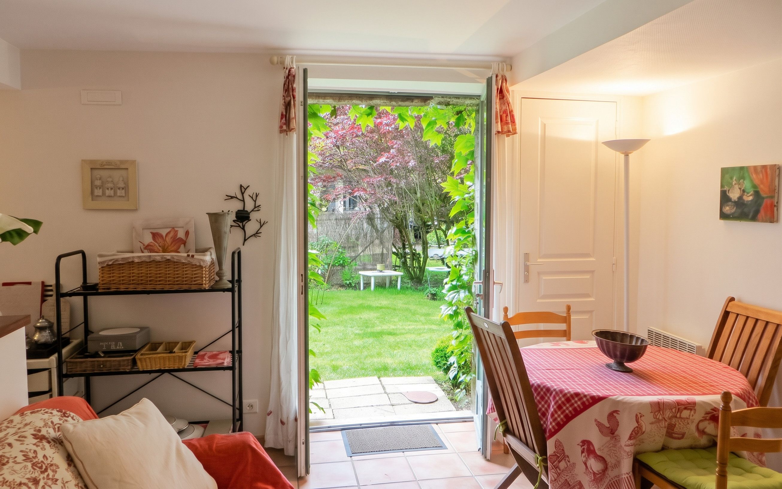 A cozy living room with a dining area, a view of a garden, and a door leading outside.
