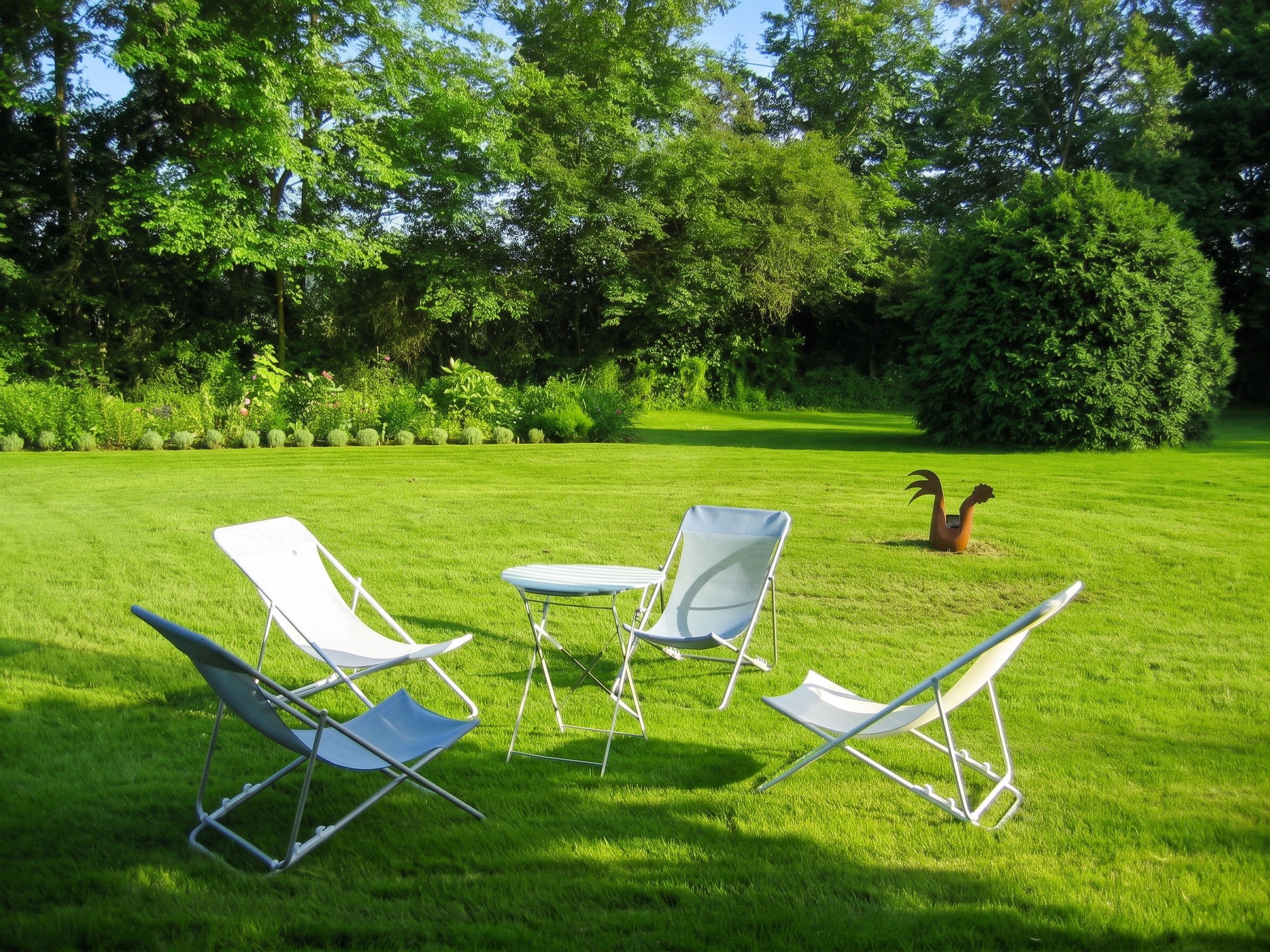 A grassy outdoor area with four white lawn chairs and a small table.