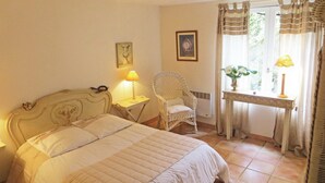 A bedroom with a bed, a chair, a table, and a window with curtains. - Homerez - House in Saint Branchs (Saint Branchs)