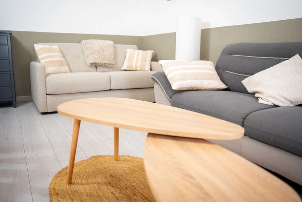 Un salon avec un canapé gris, un canapé beige, une table basse en bois et un tapis tissé.