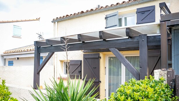 A residential building with a covered porch, a door with a window, and a small garden area with plants. - Homerez - House in Saint-Cyprien (Saint-Cyprien Plage)