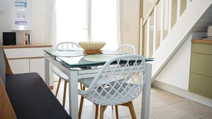 A modern kitchen with a glass table, white chairs, and a staircase. - Homerez - House in Saint-Cyprien (Saint-Cyprien Plage)