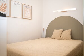 Une chambre à coucher avec un lit, une tête de lit, deux œuvres d’art encadrées et une table de chevet.