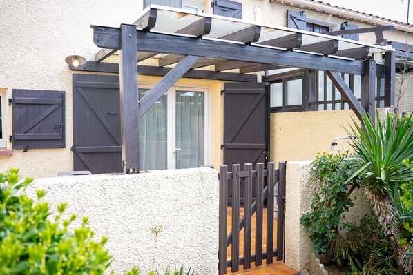 Une maison dotée d’un patio couvert, d’une entrée sécurisée par un portail et de murs extérieurs blancs.