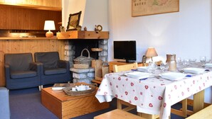 Ein gemütliches Wohnzimmer mit Kamin, Fernseher und einem für eine Mahlzeit gedecktem Esstisch.