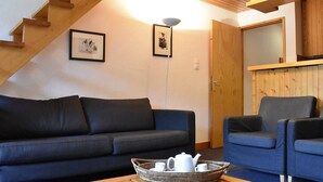 Ein gemütliches Wohnzimmer mit einem dunkelblauen Sofa, einem blauen Sessel und einem Holztisch mit einem Buch und einer Korb voller Teeutensilien.