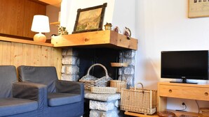 Ein gemütliches Wohnzimmer mit Kamin aus Stein, einem blauen Sofa, Korbwannen und einem Flachbildfernseher.