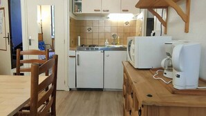 A compact kitchen with a refrigerator, microwave, and coffee maker. There is a wooden table and chairs, and a small cabinet above the sink. - 2-Room Apartment 4 Pers | Center Cauterets (Cauterets)