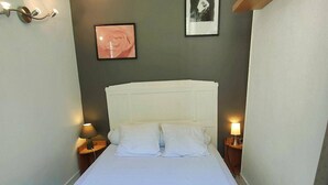 A neatly made bed with white linens, two bedside lamps, and framed pictures on the wall. - 2-Room Apartment 4 Pers | Center Cauterets (Cauterets)