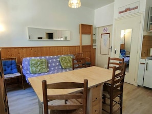 A compact room with a wooden bench, a small table, and chairs. There is a door with a sign, a mirror, and a small kitchenette area. - 2-Room Apartment 4 Pers | Center Cauterets (Cauterets)