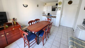 A compact kitchen with a dining table, chairs, a microwave, and a refrigerator. - Charming T3 Apartment near Wild Coast, Pool, and Beaches (Les Sables-d'Olonne)