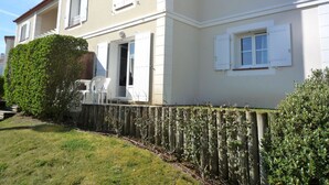 A two-story house with white shutters, a wooden fence, and a well-maintained lawn. - Charming T3 Apartment near Wild Coast, Pool, and Beaches (Les Sables-d'Olonne)