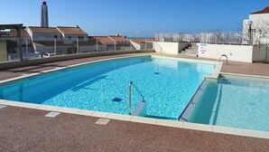A swimming pool with a clear blue water, surrounded by a white fence, and a view of buildings in the background. - Charming T3 Apartment near Wild Coast, Pool, and Beaches (Les Sables-d'Olonne)