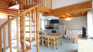 A spacious living area with a wooden staircase, a dining table, and a kitchen in the background.