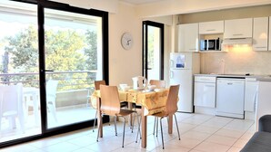 A modern kitchen with white appliances, a dining area with a table and chairs, and a large sliding glass door leading to an outdoor balcony. - Modern Apartment, 2 Bedrooms, Terrace, A/C, Parking, Near Beach, Cavalaire (Cavalaire-sur-Mer)