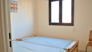 A small, simple room with a single bed, a window, and a chair. - Modern Apartment, 2 Bedrooms, Terrace, A/C, Parking, Near Beach, Cavalaire (Cavalaire-sur-Mer)
