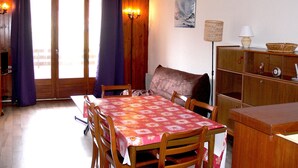 A dining area with a table set for four, wooden chairs, a sofa, a cabinet, and a lamp. - Charming Ski-In Apartment, Sleeps 6, South-Facing Balcony, Ideal for Families - Peyragudes (Gouaux-de-Larboust-Les Agudes)