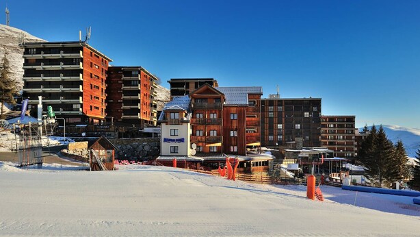 A ski resort with multi-story buildings, including a hotel with a wooden facade and a modern building with a red facade. - Charming Ski-In Apartment, Sleeps 6, South-Facing Balcony, Ideal for Families - Peyragudes (Gouaux-de-Larboust-Les Agudes)