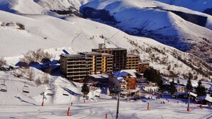 A snow-covered mountain resort with a multi-story building featuring balconies, ski lifts, and a ski slope. - Charming Ski-In Apartment, Sleeps 6, South-Facing Balcony, Ideal for Families - Peyragudes (Gouaux-de-Larboust-Les Agudes)