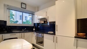 A modern kitchen with white cabinets, a black countertop, a stainless steel oven, and a window with a view of buildings outside. - N&J - L'OLYMPIC - Central - Very close sea (Niza)
