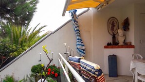 A covered outdoor seating area with a white chair, a table, and a potted plant.