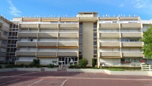 A multi-story building with a central vertical structure, balconies on each floor, and a parking area in front. - Charming 1-Bed Apt with South-Facing Terrace, Beach Access & Parking in Arcachon (Arcachon)