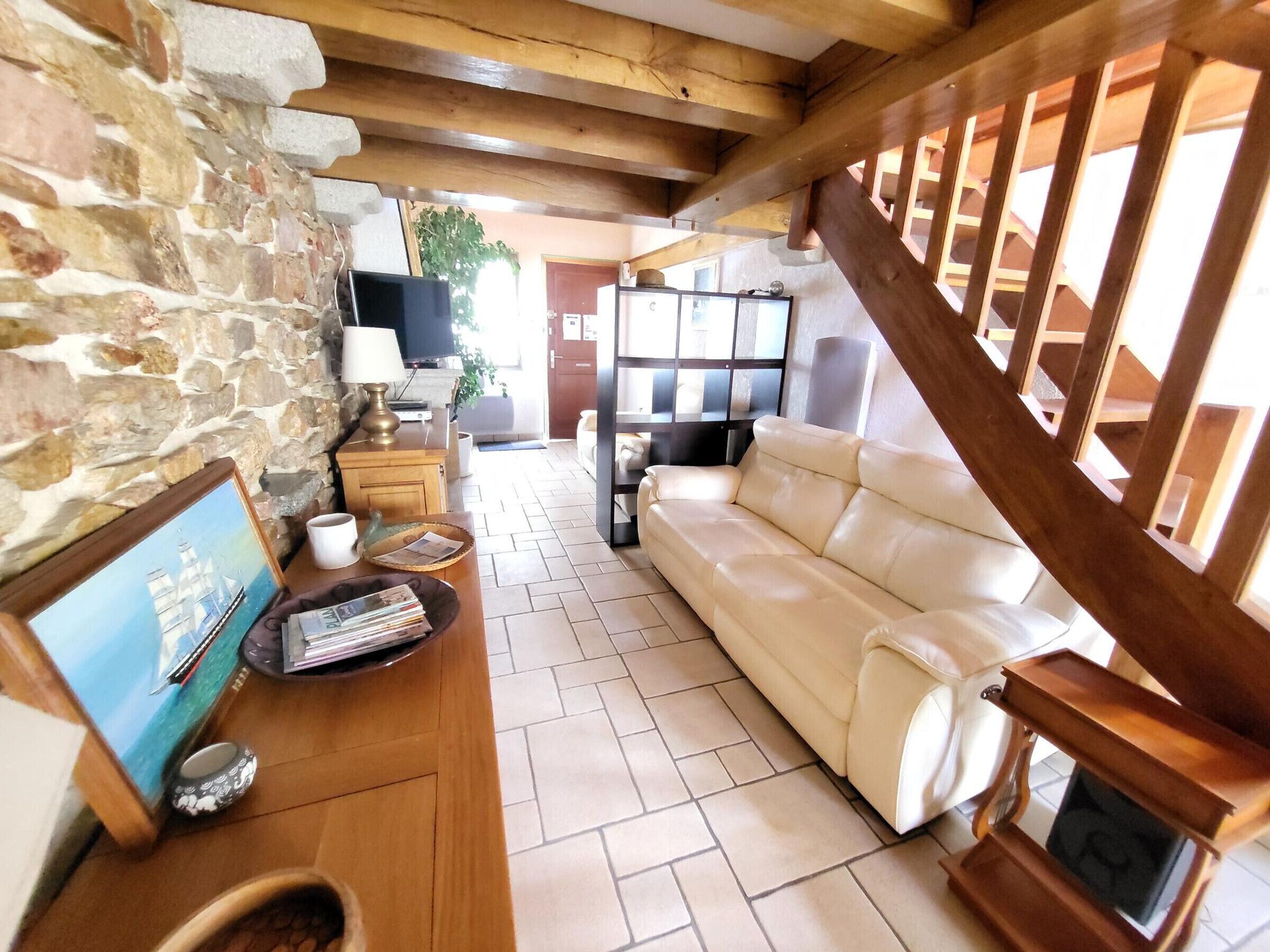Un salon avec un mur en pierre, un plafond en bois, un canapé blanc, une table basse en bois et un téléviseur.
