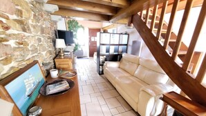 Una sala de estar con una pared de piedra, techo de madera, un sofá blanco, una mesa de centro de madera y un televisor.