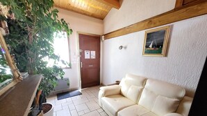 Una habitación con un sofá color beige, techo de madera, una puerta con un aviso y un cuadro en la pared.
