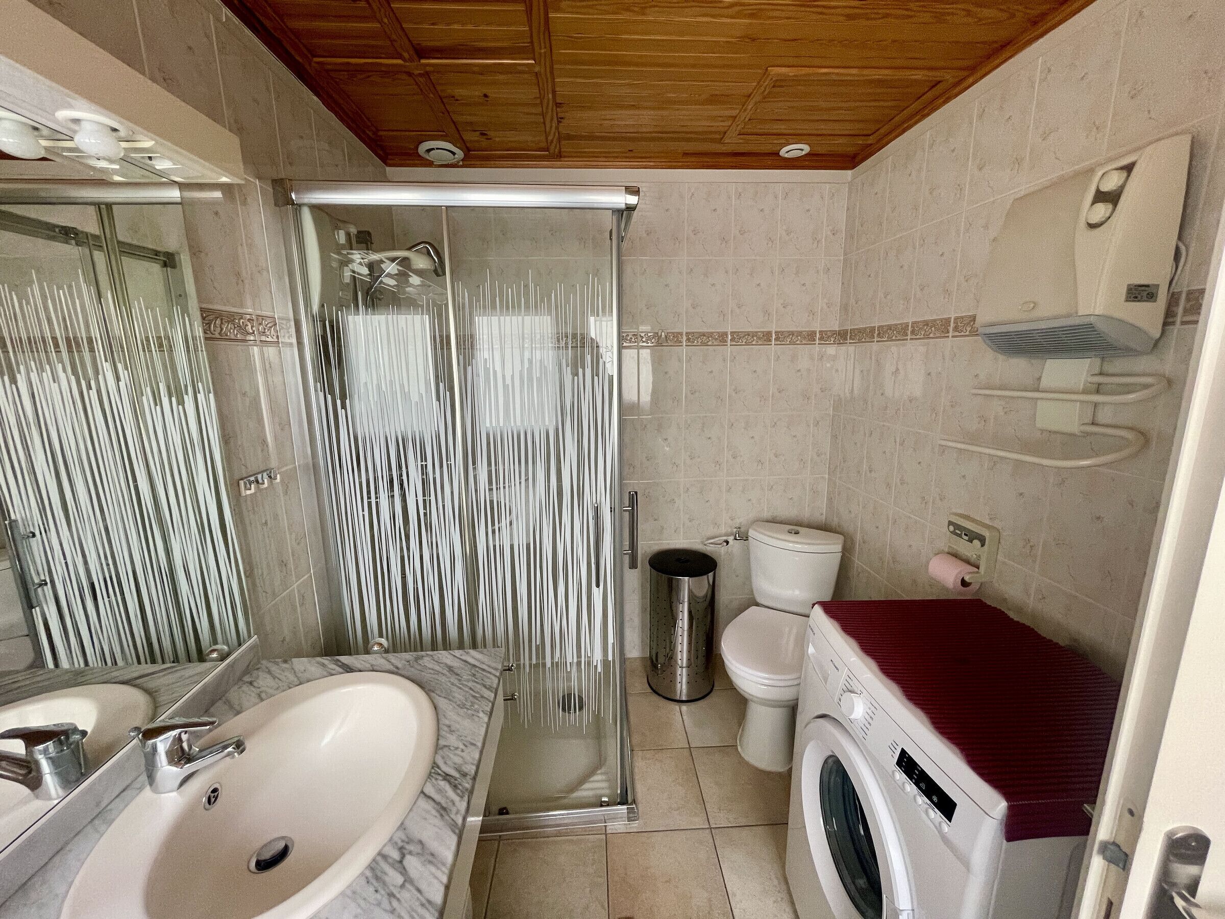 Ein Badezimmer mit Dusche, Toilette, Waschbecken und Waschmaschine.