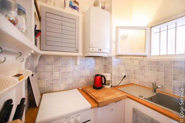 Een kleine keuken met een witte kookplaat, een houten aanrecht, een spoelbak en een raam.