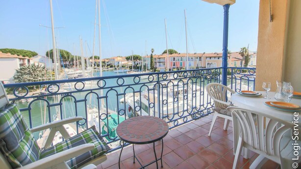 Un balcon donnant sur un port de plaisance, avec des meubles d’extérieur blancs et une table carrelée.