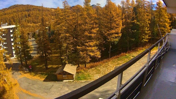 A view of a building with multiple floors and a balcony overlooking a forested area with autumn-colored trees.