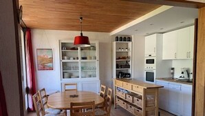 A compact kitchen with white cabinets, a wooden dining table with chairs, and a red pendant light.