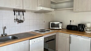 Eine kompakte Küche mit weißen Schränken, einer Mikrowelle, einem Toaster, einer Kaffeemaschine und einem Geschirrspüler.