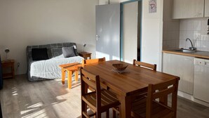Ein gemütlicher Raum mit einem Bett, einem Esstisch mit Stühlen, einer kleinen Küchenzeile und einer Tür zu einem weiteren Raum.