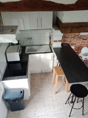 Une cuisine de taille réduite avec des meubles blancs, un plan de travail noir et un tabouret en bois.
