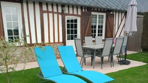 Patio con una mesa de comedor y sillas, dos sillones azules y un árbol pequeño.