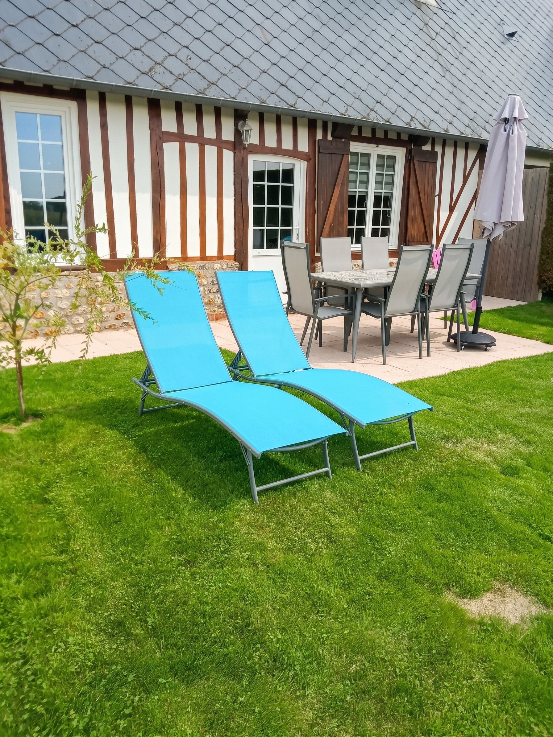 A patio with two blue lounge chairs, a table, and chairs.