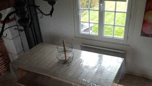 Una habitación con una mesa de madera cubierta con plástico, una lámpara de metal y una ventana con persianas.