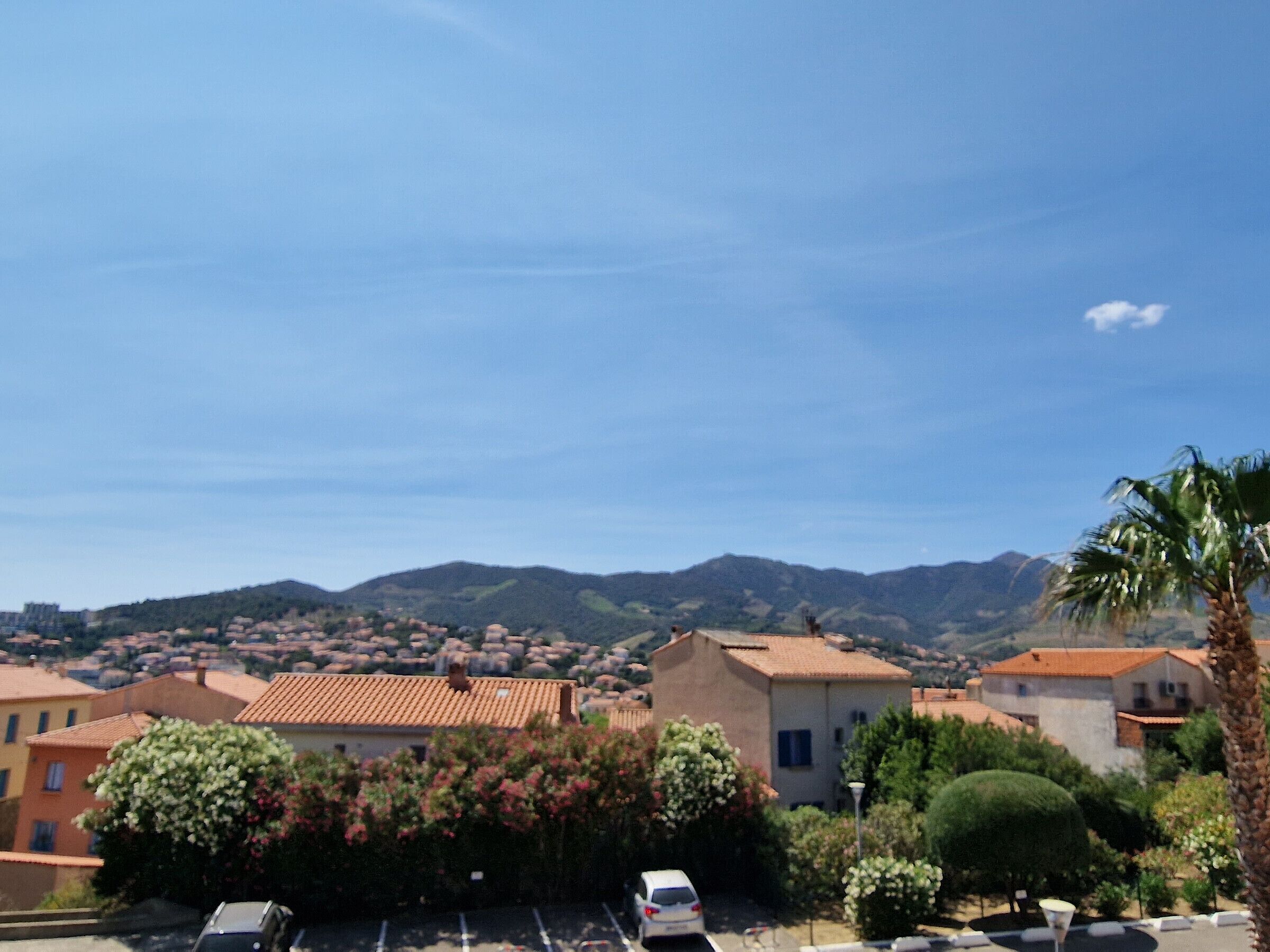 A residential area with buildings, a parked car, and mountains in the background.